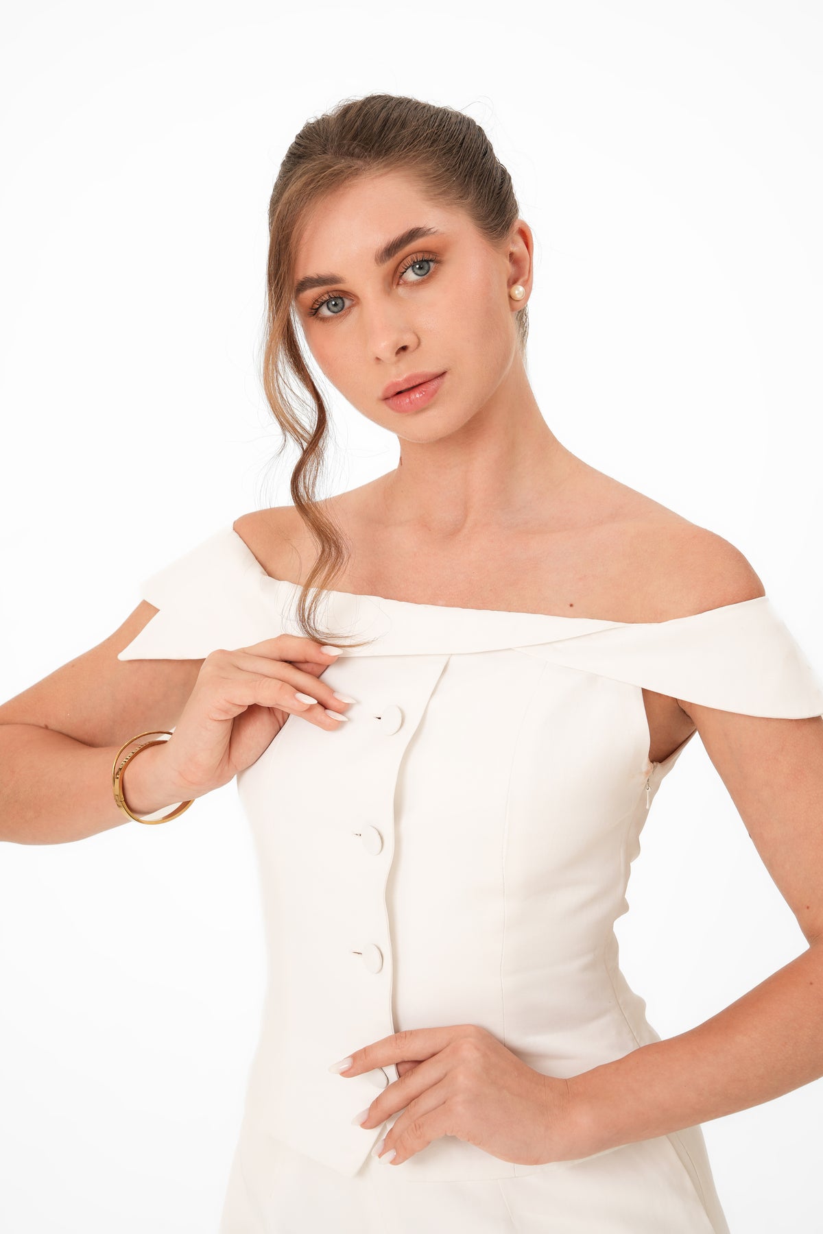 A woman modeling an off-the-shoulder white dress with a buttoned front panel, photographed against a clean white studio background.