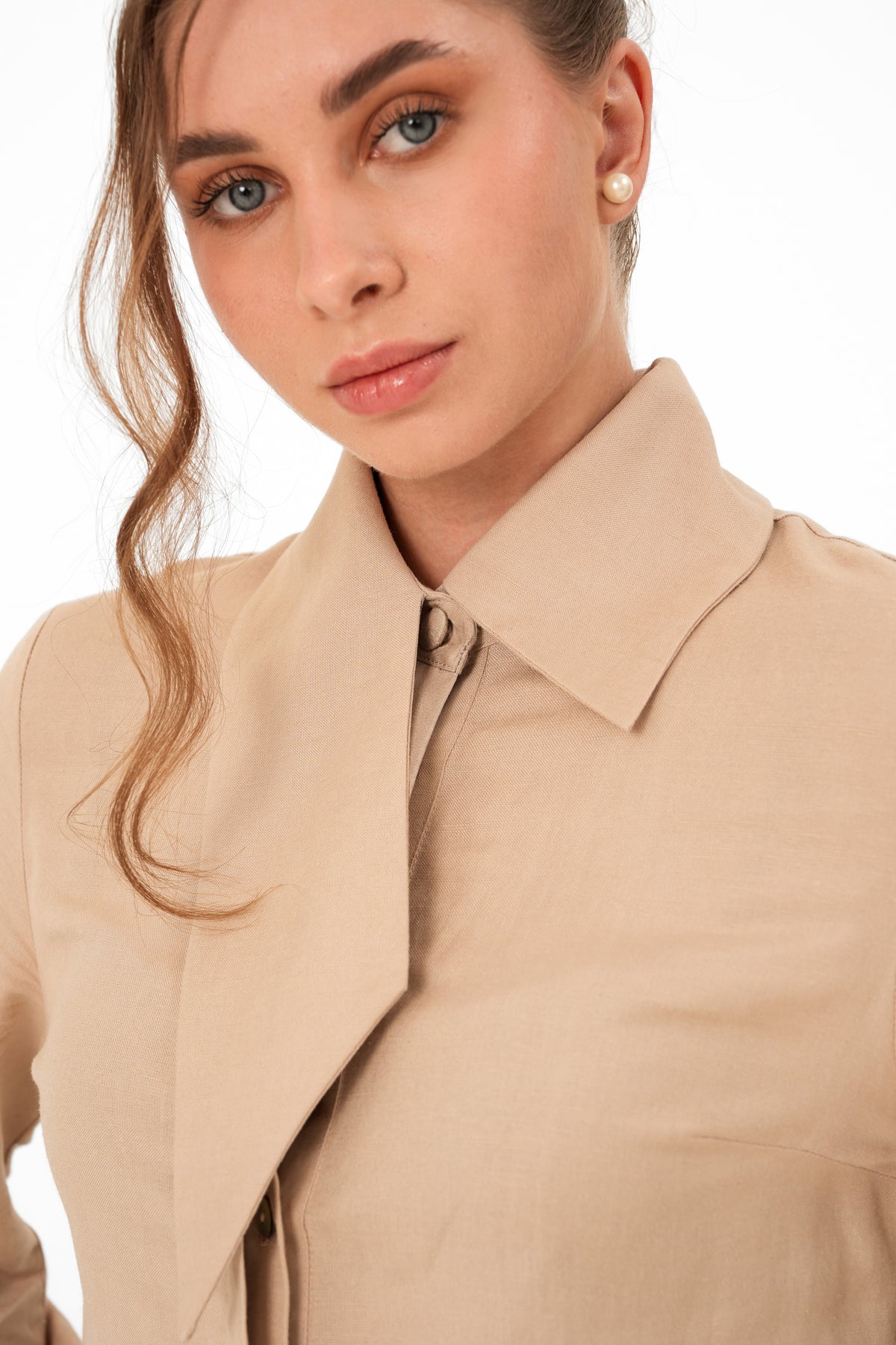 Close-up of a woman wearing a beige collared blouse or shirt against a plain white background.