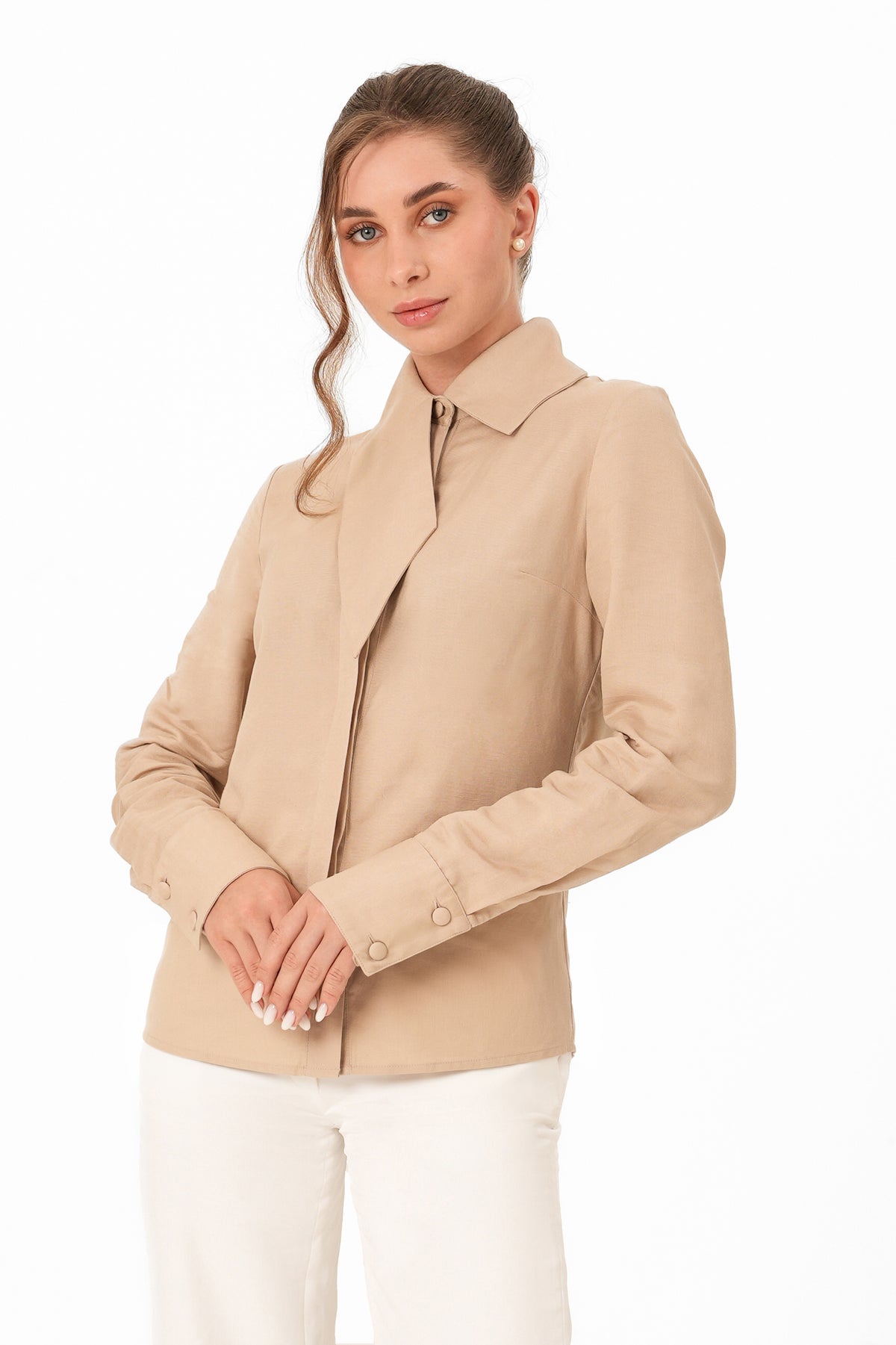 A woman modeling a beige structured jacket with a collar and front buttons, paired with white pants, against a plain white background.