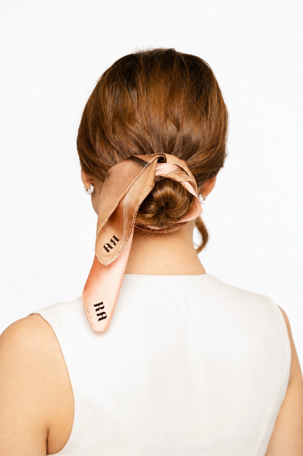 A woman shown from the back wearing a peach-colored satin hair tie with black lettering, styled in a low bun.