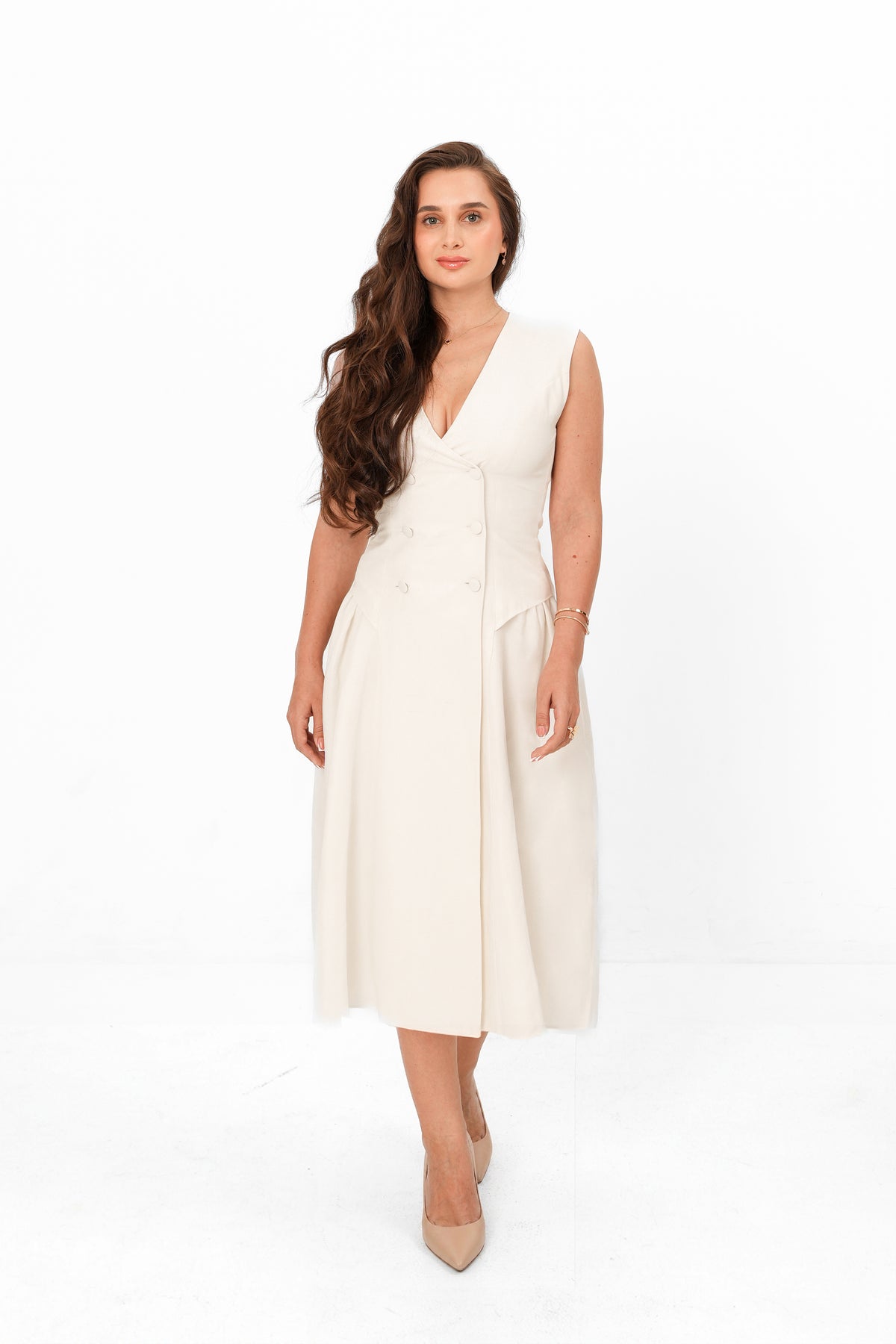 A woman modeling a sleeveless cream midi dress with a V-neckline and button-front detail, standing against a plain white studio background.