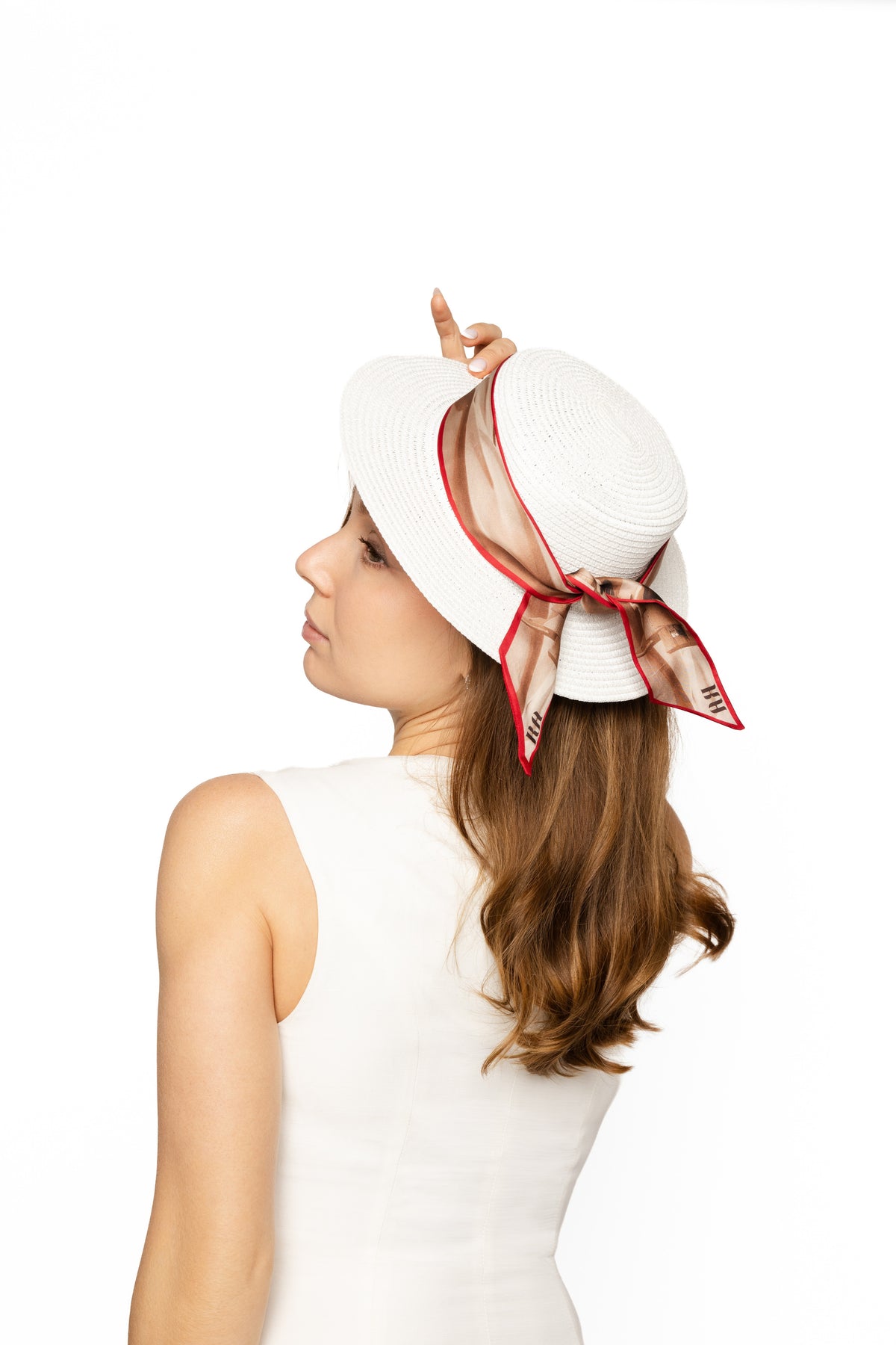 A woman in a white sleeveless dress shown from the back and side, wearing a white wide-brim sun hat with a red-trimmed scarf tied in a bow on the side, against a plain white background.