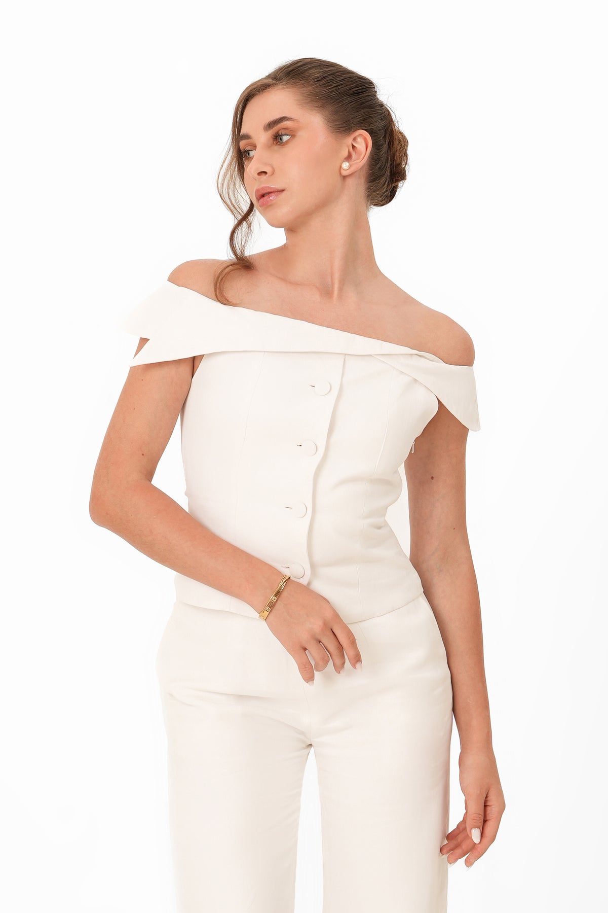A woman modeling an off-the-shoulder white jumpsuit with a structured bodice, front buttons, and matching fitted pants against a plain white background.