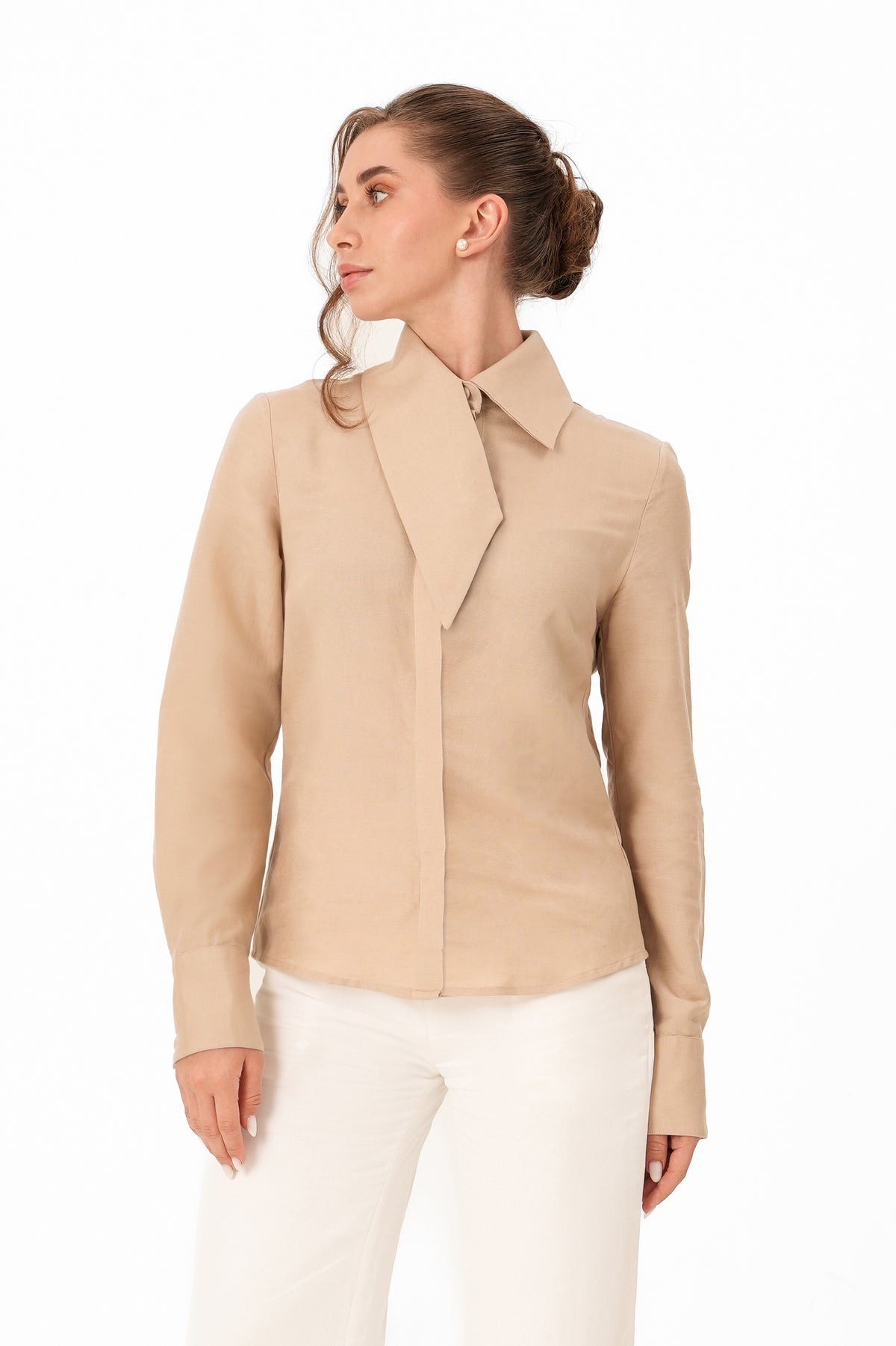 A woman wearing a beige long-sleeve collared blouse with a unique draped front detail, paired with white pants, photographed against a plain white background.