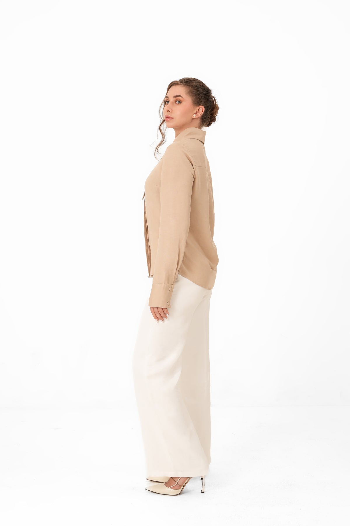 A woman shown in side profile wearing a beige cropped cardigan and a long cream skirt against a plain white studio background.