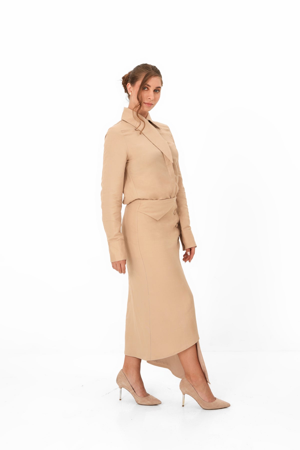 A woman modeling a beige long-sleeve wrap-style midi dress with a matching belt, paired with beige high heels, against a plain white studio background.