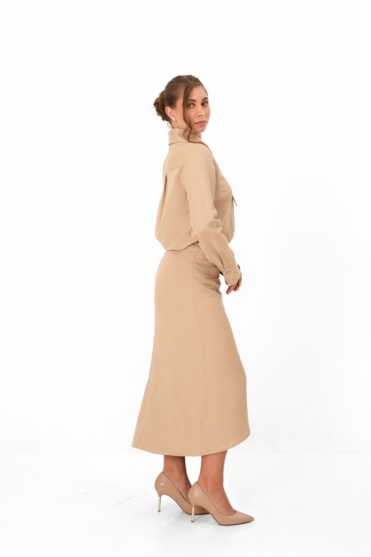 A woman modeling a beige long-sleeve mock-neck top and matching midi skirt set, paired with beige high heels, against a plain white studio background.